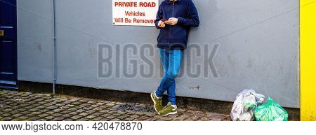 Low-section Of Young Man Reading Using Smartphone Telephone Next To Private Road Vehicles Will Be Re