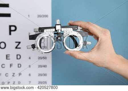 Woman Holding Trial Frame Against Eye Chart Test On Blue Background, Closeup. Ophthalmologist Tool