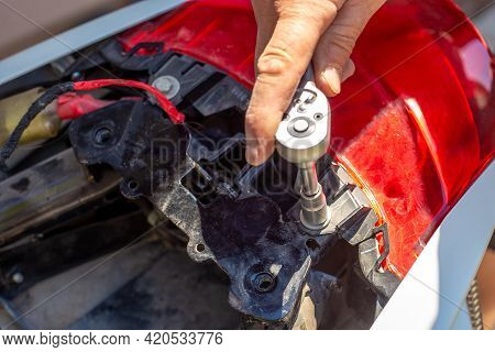 Repair And Dismantling Of A Motorcycle. A Man Unscrews The Trunk Fasteners With A Socket Wrench.