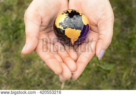 The Earth Globe Is Safely Held Inside The Palm Of A Womans Hands Overtop Of A Grass Area.