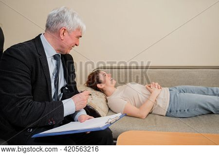 Caucasian Woman Lies On A Couch At A Reception With A Psychotherapist. An Elderly Man Works As A Psy