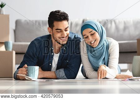 Happy Middle-eastern Couple Laying On Floor With Apartment Plan