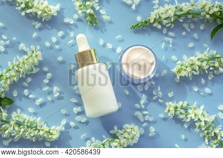 White Bottle Of Cosmetic Serum And Cream Jar On Teal Blue Background With Byttneria Flowers. Natural
