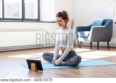 fitness, people and healthy lifestyle concept - young woman with tablet pc computer doing yoga at home