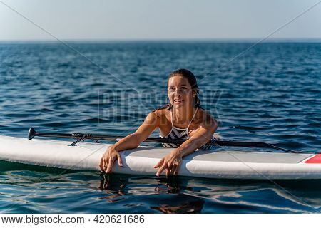 Sporty Girl On A Glanders Surfboard In The Sea On A Sunny Summer Day. In A Striped Swimsuit, He Lies