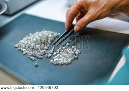 Manual Sorting Of Diamonds. A Hand With Tweezers Transfers Diamonds From One Pile To Another.