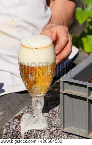 A Man With One Glass Of Beer Beside Hime While Woking In The Garden In Sunny Day For Refreshing.