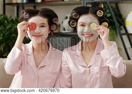 Portrait Of Young Joyful Women Applying Clay Masks And Vegetable Slices On Faces