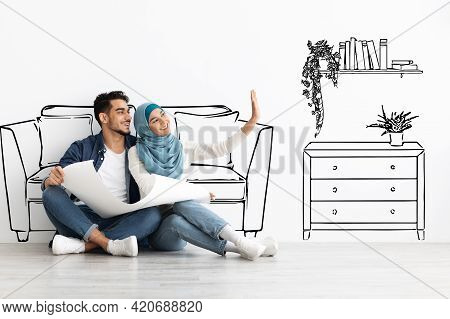 Happy Arab Couple Sitting On Floor In Empty Apartment