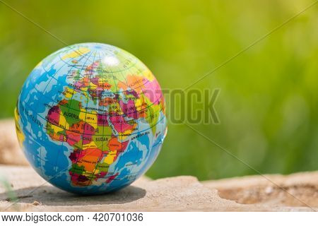 Toy Ball, Globe Of The Planet Earth On A Wooden Stump In A Forest On A Green Grass Background. Trave