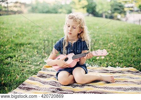 Cute Adorable Blonde Girl Playing Pink Guitar Toy Outdoors. Child Playing Music And Singing Song In 