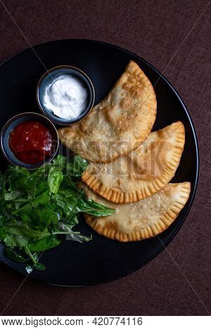 Appetizing Fried Chebureks On A Black Plate With Greens