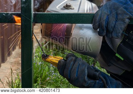 Worker Male Welder At A Construction Site Welds A Metal Structure On A Fence, Welding Process Close-