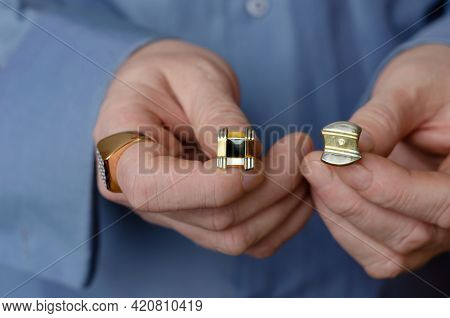 Concept Of Choice. Close-up Of Hands Holding Two Different Cufflinks. A Middle-aged Adult Man With A