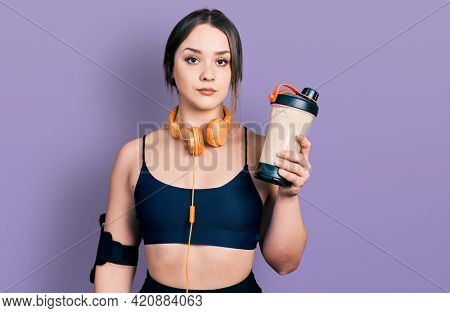 Young hispanic girl wearing sport clothes drinking a protein shake thinking attitude and sober expression looking self confident 