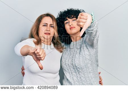 Middle east mother and daughter wearing casual clothes looking unhappy and angry showing rejection and negative with thumbs down gesture. bad expression. 