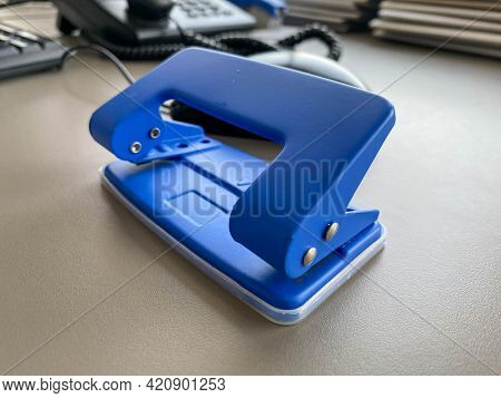 Blue Iron Metal Office Punch For Punching Holes In Sheets Of Paper And Documents On The Working Busi