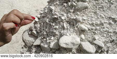 Female Hand Holding A Piece Of Chalk Of A White Rock. Small Smooth Calcite Stones Are Mixed With Cha