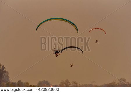 Silhouette Of The Paramotor Gliding And Flying In The Air Through Soft Sunlight Sky. Paramotor It Is