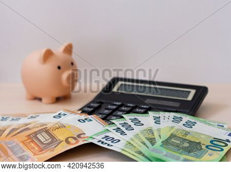 A Piggy Bank, A Calculator And Paper Money In Denominations Of 100 And 50 Euros, Spread Out In A Fan