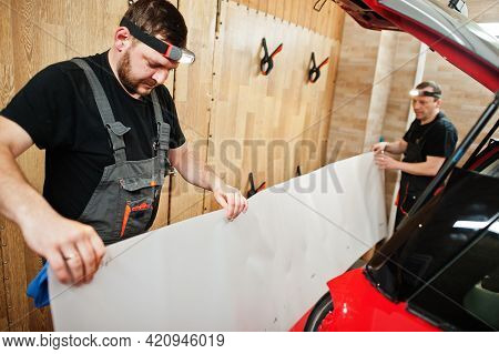 Car Service Worker Put Anti Gravel Film On A Red Car Body At The Detailing Vehicle Workshop. Car Pro
