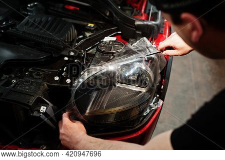 Car Service Worker Put Anti Gravel Film On A Red Car Body At The Detailing Vehicle Workshop. Car Pro