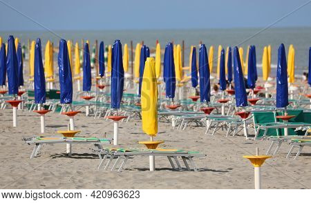 Beach With Closed Umbrellas With No One On The Deck Chairs Due To The Lockdown