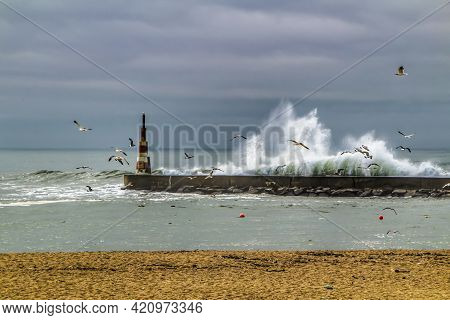 Giant Waves Breaking On The Breakwater And The Lighthouse On Aguda Beach, Miramar, Arcozelos Town