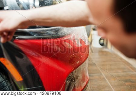 Car Service Worker Put Anti Gravel Film On A Red Car Body At The Detailing Vehicle Workshop. Car Pro