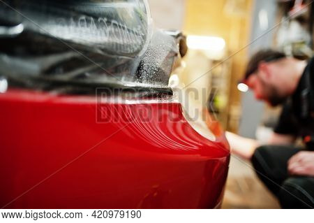 Car Service Worker Put Anti Gravel Film On A Red Car Body At The Detailing Vehicle Workshop. Car Pro