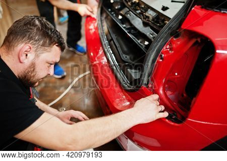 Car Service Worker Put Anti Gravel Film On A Red Car Body At The Detailing Vehicle Workshop. Car Pro