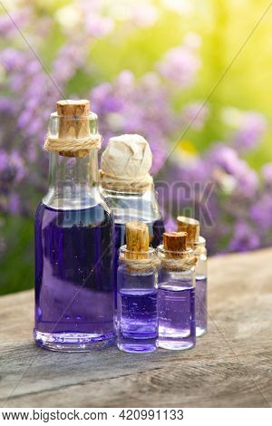 Glass bottle of Lavender essential oil on wood table and flowers field. Lavendula oleum
