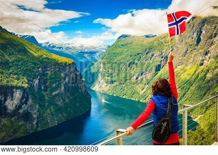 Female Tourist With Norwegian Flag Enjoying Scenic View Over Fjord Geirangerfjord With Ferry Boat An