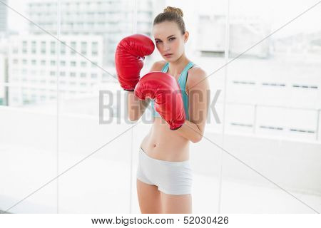 Sporty serious woman wearing boxing gloves in bright room
