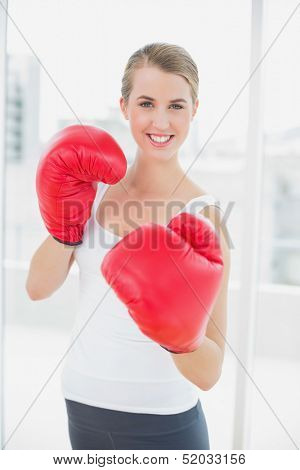 Smiling fit woman with red gloves boxing in bright sports hall