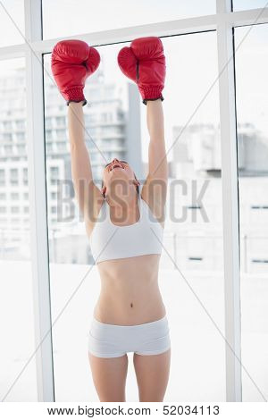 Delighted fit brown haired model in sportswear wearing red boxing gloves in bright fitness studio