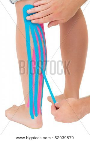 Physiotherapist applying pink and blue kinesio tape on patients leg on white background