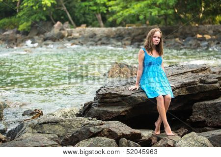Teengirl in a blue dress in the rocks of the coast.