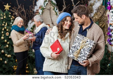 Happy young couple holding Christmas presents with parents standing in background at store