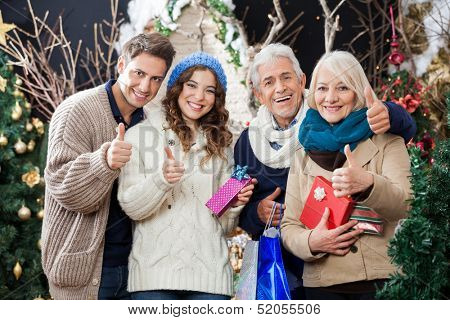 Portrait of happy family with Christmas presents and shopping bags gesturing thumbs up in store