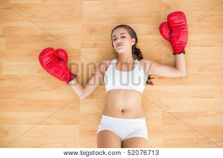 Sporty tired brunette wearing red boxing gloves and lying on the floor