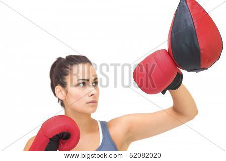 Serious sporty brunette training with punching bag on white background