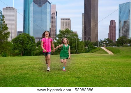 Two sister girls friends running holding hand in urban modern skyline on grass lawn
