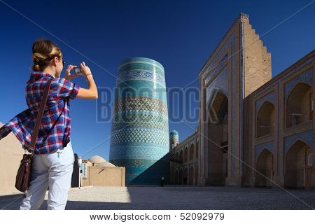 Young lady taking a picture of oriental buildings in Itchan Kala ancient town. Khiva, Uzbekistan