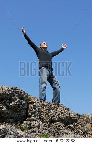 A man standing on a cliff with his arms raised to the blue sky