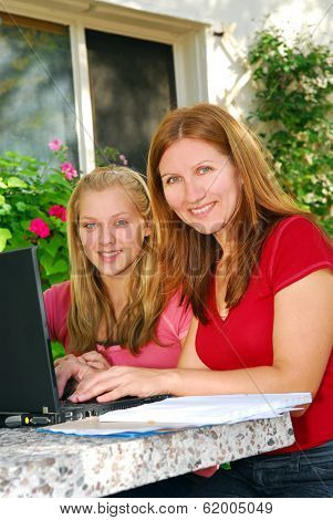 Mother and daughter working on computer at home in the backyard