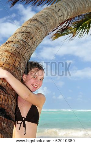 Happy young girl higging a palm tree on tropical beach