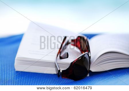 Sunglasses and open book on beach chair - summer vacation concept