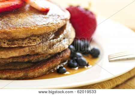 Stack of buckwheat pancakes with fresh berries and maple syrup