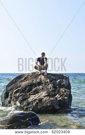 Man stranded on a rock in ocean waiting for rescue
